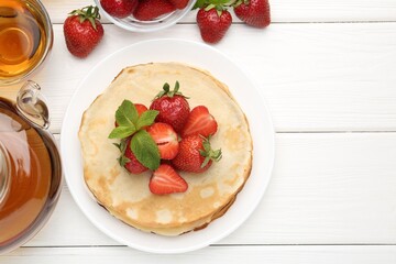 Delicious crepes with strawberries, mint and tea on white wooden table, flat lay