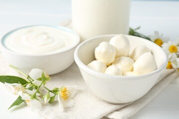 Fresh dairy products and flowers on white wooden table, closeup