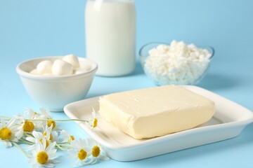 Fresh dairy products and chamomile flowers on light blue background, closeup
