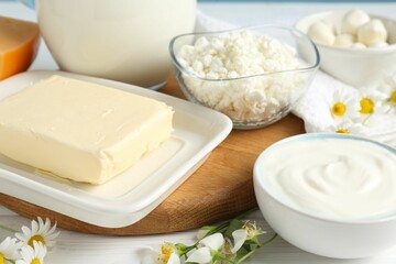 Fresh dairy products and flowers on white wooden table, closeup