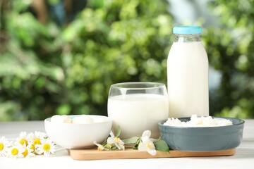 Different fresh dairy products and flowers on white wooden table outdoors
