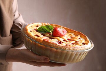 Woman holding tasty strawberry pie on light brown background, closeup