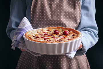 Woman holding tasty cherry pie on black background, closeup