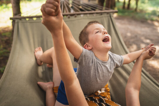 Emotional Mother and son are fooling around in a hammock in the summer forest. Family outdoor recreation, hugs, emotions. Time spent together