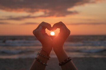 silhouette of a pair of hands creating a heart on the beach near ocean with sun set in between