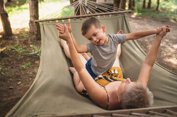 Emotional Mother and son are fooling around in a hammock in the summer forest. Family outdoor...