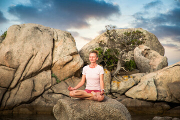 woman meditating on rock on the beach