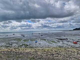 Coastal low tide landscape with stranded boats under dramatic cloudy sky, France, Normandy