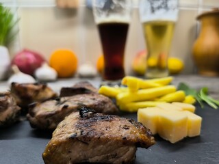 Delicious pieces of shish kebab lie on a sliced board with French fries. There are glasses of dark...