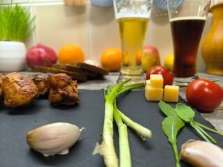 Fried chicken pieces lie on a sliced board next to glasses of beer