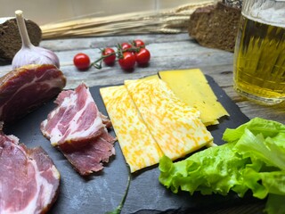 juicy sliced ​​piece of dried meat on a cutting board, next to it green salad leaves, cheese...