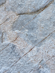A close-up of a natural stone surface in cool gray tones, accented with fine reddish veins and scattered mineral speckles.