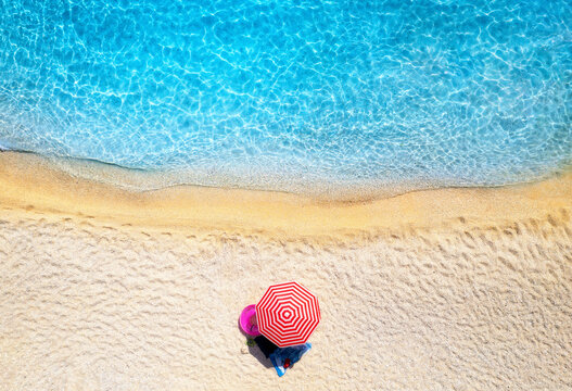 Fototapeta Aerial view of red umbrella, sandy beach, blue sea, waves at sunset in summer. Tropical landscape with seashore, clear turquoise water. Top view from drone. Lefkada island, Greece. Travel