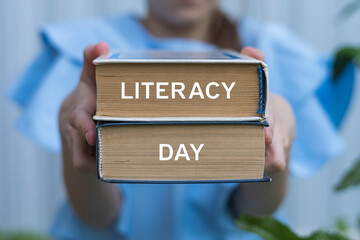Young girl holding two books with inscription on side: LITERACY DAY. International Literacy Day...