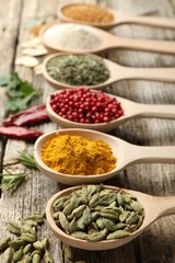 Different aromatic spices in spoons on wooden table, closeup