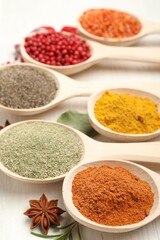 Different aromatic spices in spoons on white wooden table, closeup