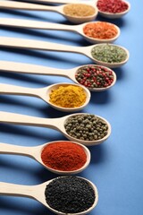 Different aromatic spices in spoons on blue background, closeup