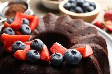 Tasty chocolate bundt cake with berries on table, closeup
