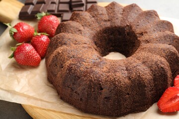 Tasty bundt cake, chocolate pieces and strawberries on grey table, closeup