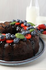 Delicious chocolate bundt cake with strawberries, mint and blueberries on light wooden table, closeup