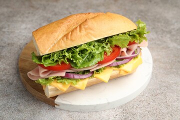 Tasty baguette sandwich with ham, cheese and vegetables on grey textured table, closeup