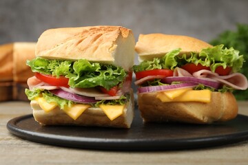 Pieces of tasty baguette sandwich with ham, cheese and vegetables on wooden table against grey background, closeup