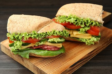 Pieces of tasty baguette sandwich with smoked sausage, cheese and vegetables on wooden table,...