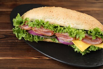 Tasty baguette sandwich with ham, cheese and vegetables on wooden table, closeup