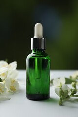 Essential oil and jasmine flowers on white table against blurred background, closeup