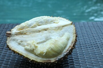 Fresh ripe durian on wicker table near swimming pool outdoors, closeup