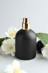 Bottle of perfume and jasmine flowers on light background, closeup