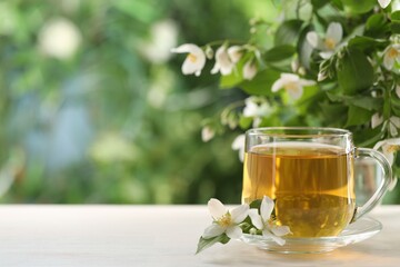 Tasty jasmine tea in cup and flowers at white wooden table, closeup. Space for text