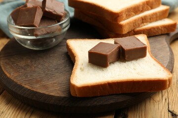Tasty chocolate butter cubes on slice of bread on wooden table, closeup