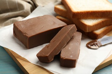 Pieces of tasty chocolate butter and slices of bread on light blue wooden table, closeup
