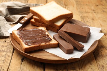 Pieces of tasty chocolate butter and slices of bread on wooden table, closeup