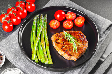 Tasty grilled beef steak served with green asparagus and cherry tomatoes on black plate, with cutlery. Perfect for food menu, diet, or culinary design concepts.