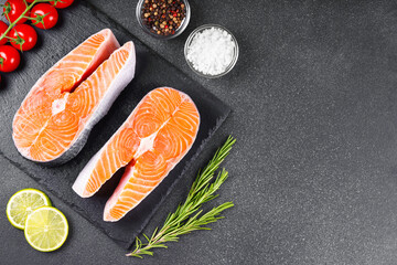 Two fresh raw salmon steaks on black stone surface with food ingredients. Tomatoes, lime, rosemary,...