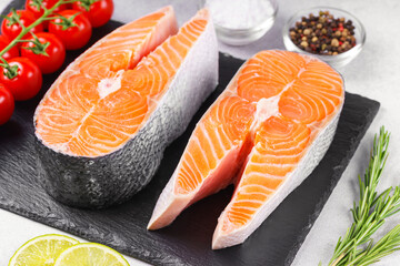 Two fresh raw salmon steaks on white stone surface with food ingredients. Tomatoes, lime, rosemary,...