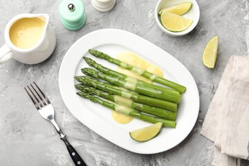 Tasty cooked asparagus served with sauce and lime on grey textured table, flat lay