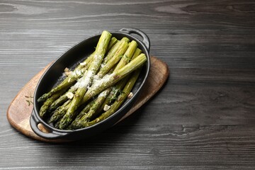 Tasty cooked asparagus served with parmesan on black wooden table, space for text