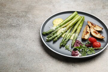 Tasty cooked asparagus served with baked potatoes, tomatoes and sauce on grey table, closeup. Space...
