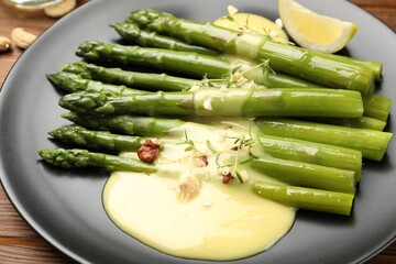 Tasty cooked asparagus served with lemon and sauce on wooden table, closeup