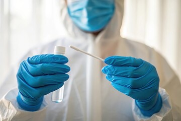 Healthcare worker in protective gear holds a testing swab and collection tube