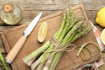 Fresh raw asparagus spears, knife, lemon and oil on wooden table, flat lay