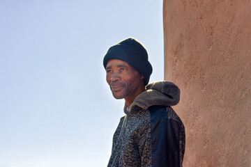 africa village, single african man with a hoodie and beanie, in the township , cold day, standing...