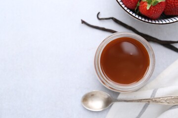 Tasty panna cotta with caramel, vanilla pods and strawberries on light table, flat lay. Space for text