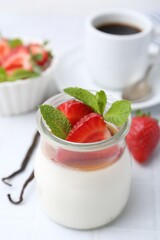 Tasty panna cotta with caramel, strawberries, mint, vanilla pods and coffee on white table, closeup