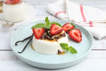 Tasty panna cotta with chocolate, strawberries, mint, caramel and vanilla pods on white wooden...