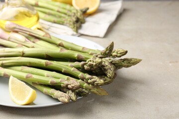 Fresh raw asparagus, oil and lemon on light grey table, closeup. Space for text