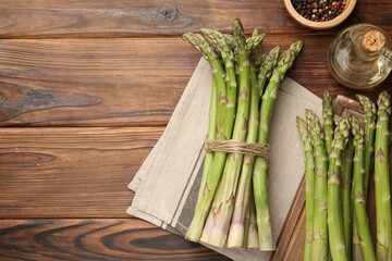 Fresh raw asparagus, spices and oil on wooden table, flat lay. Space for text